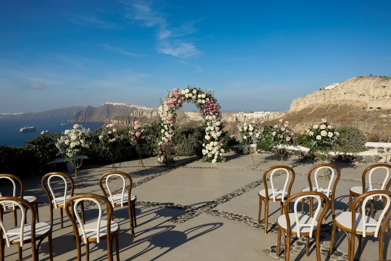 A Santorini wedding ceremony set up with a floral arch above the caldera