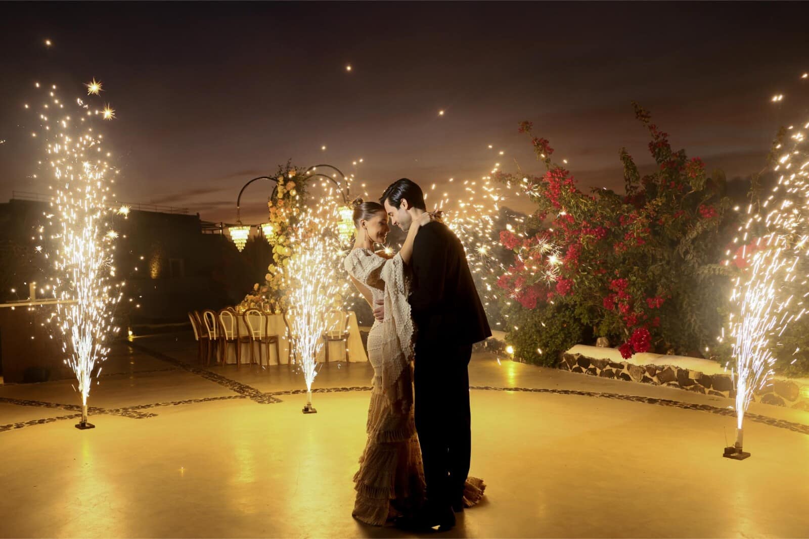 A couple dancing between fountains of sparks at a grand Santorini reception